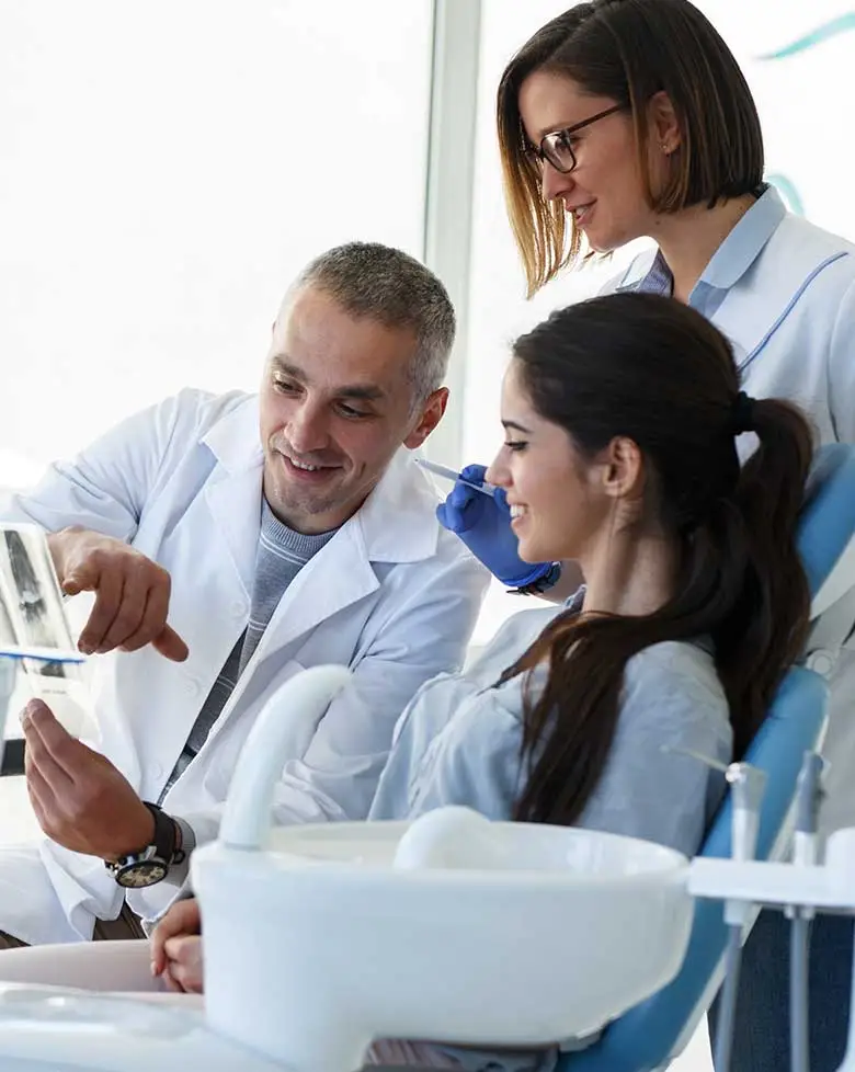 A dentist and dental assistant reviewing an image with a patient in the dental chair