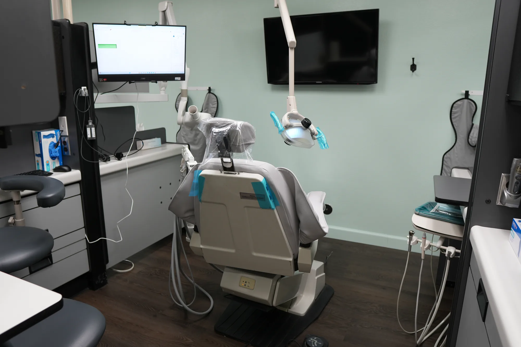 Dental exam room with a dental chair, overhead light, wall-mounted monitors and a counter
