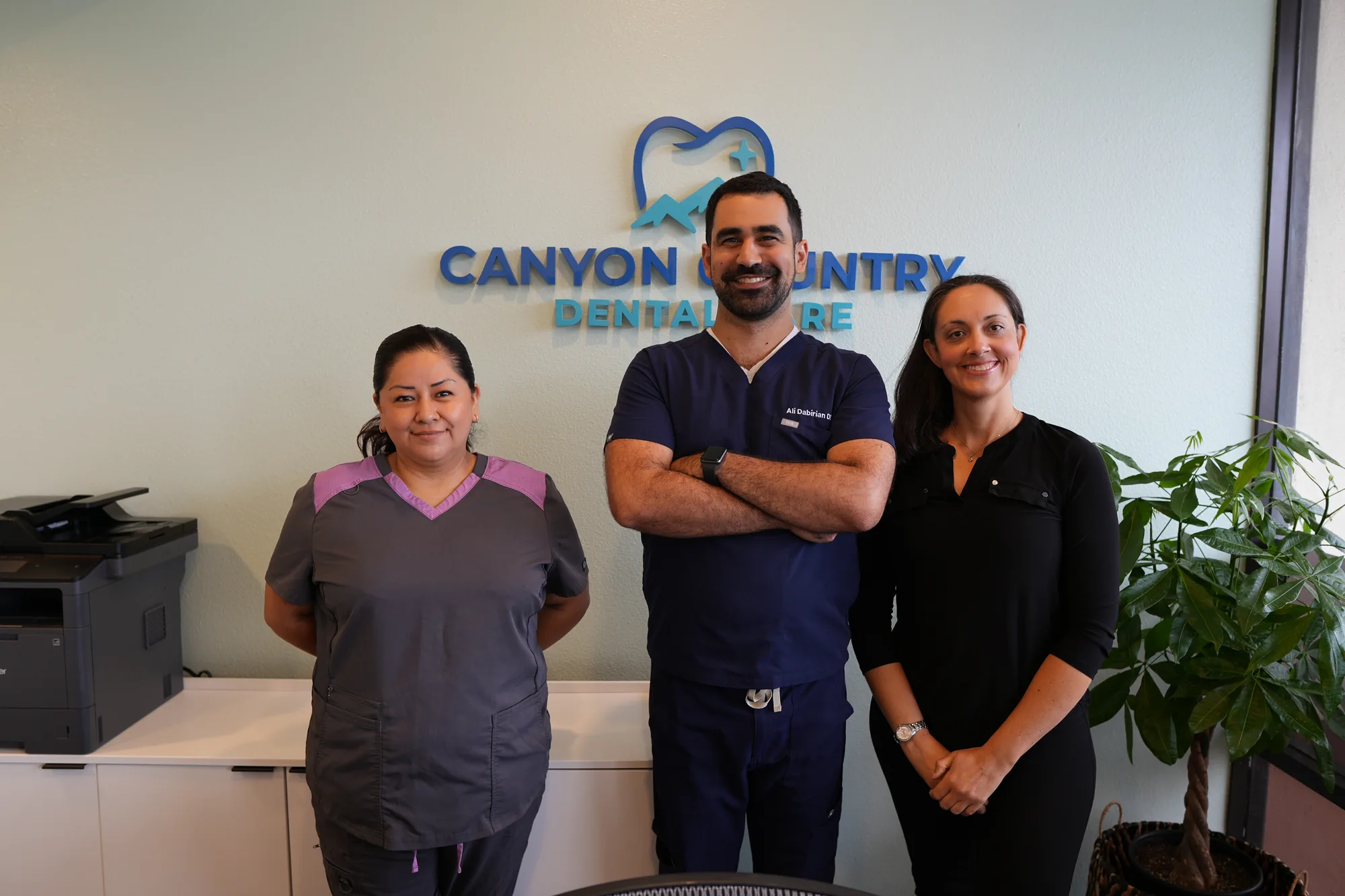 Dr. Dabirian standing with two team members in front of the Canyon Country Dental Care logo