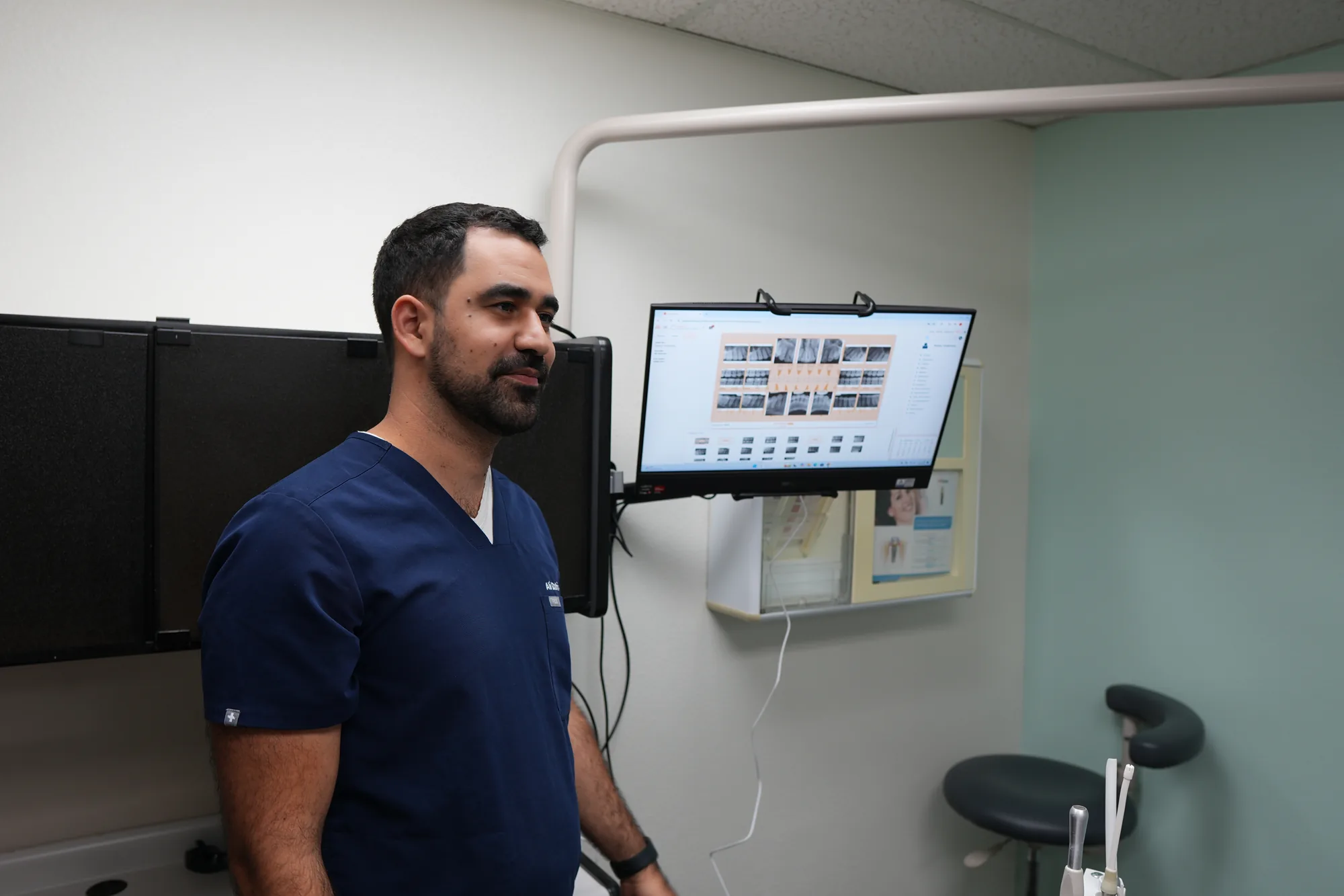 Dr. Dabirian standing next to a wall-mounted monitor displaying dental images