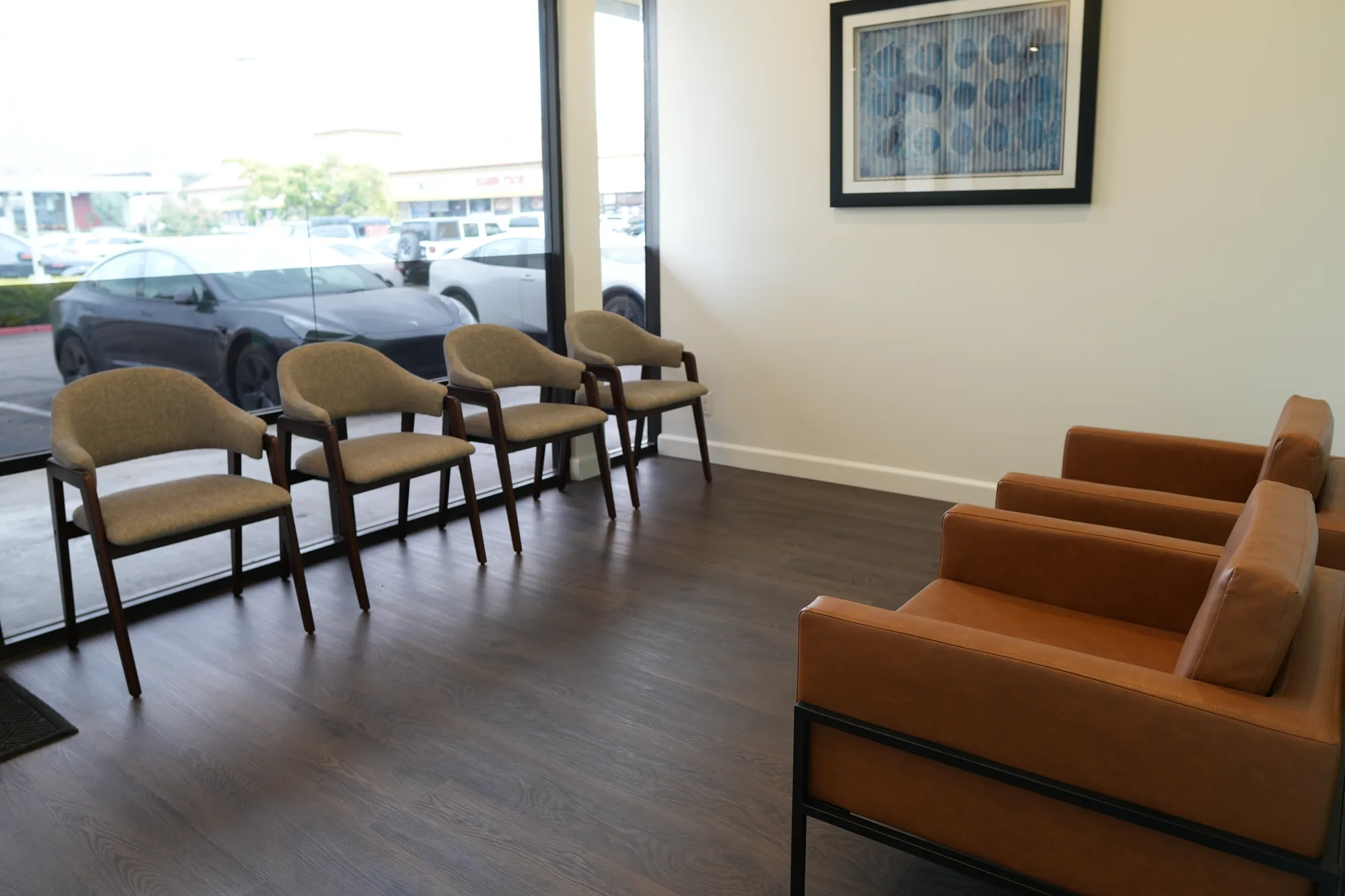 Waiting room with cushioned chairs by the window and a leather sofa beside a framed picture